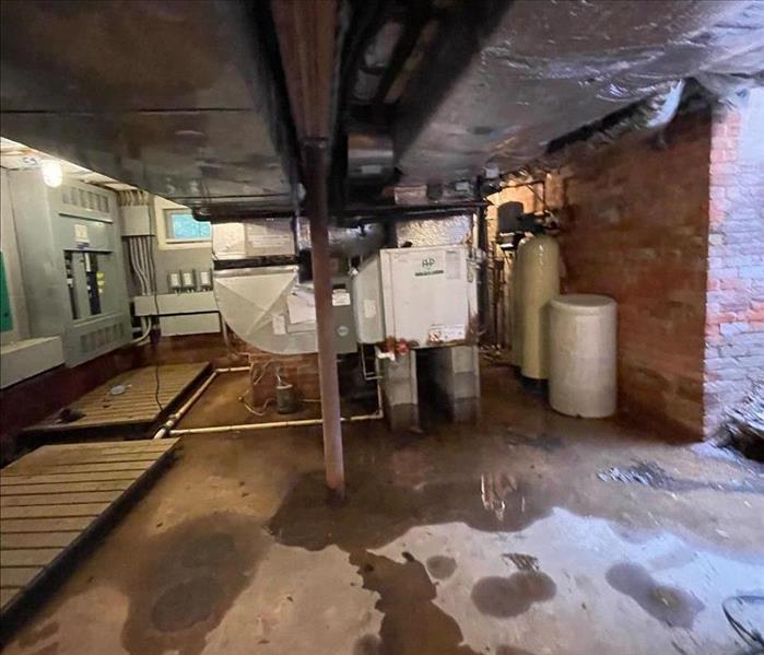 Basement with standing water on the concrete floor and lower brick wall