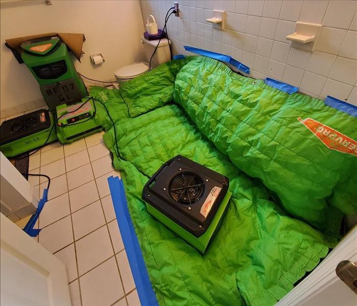Partially sealed SERVPRO Green drying pad, air movers, and a dehumidifier operating in a bathroom