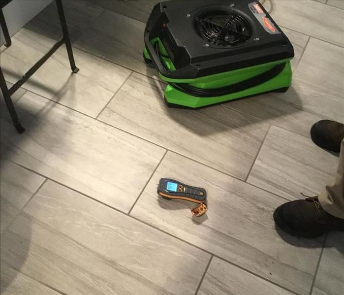 SERVPRO tech evaluates floor moisture with a non-penetrating sensor near an air mover